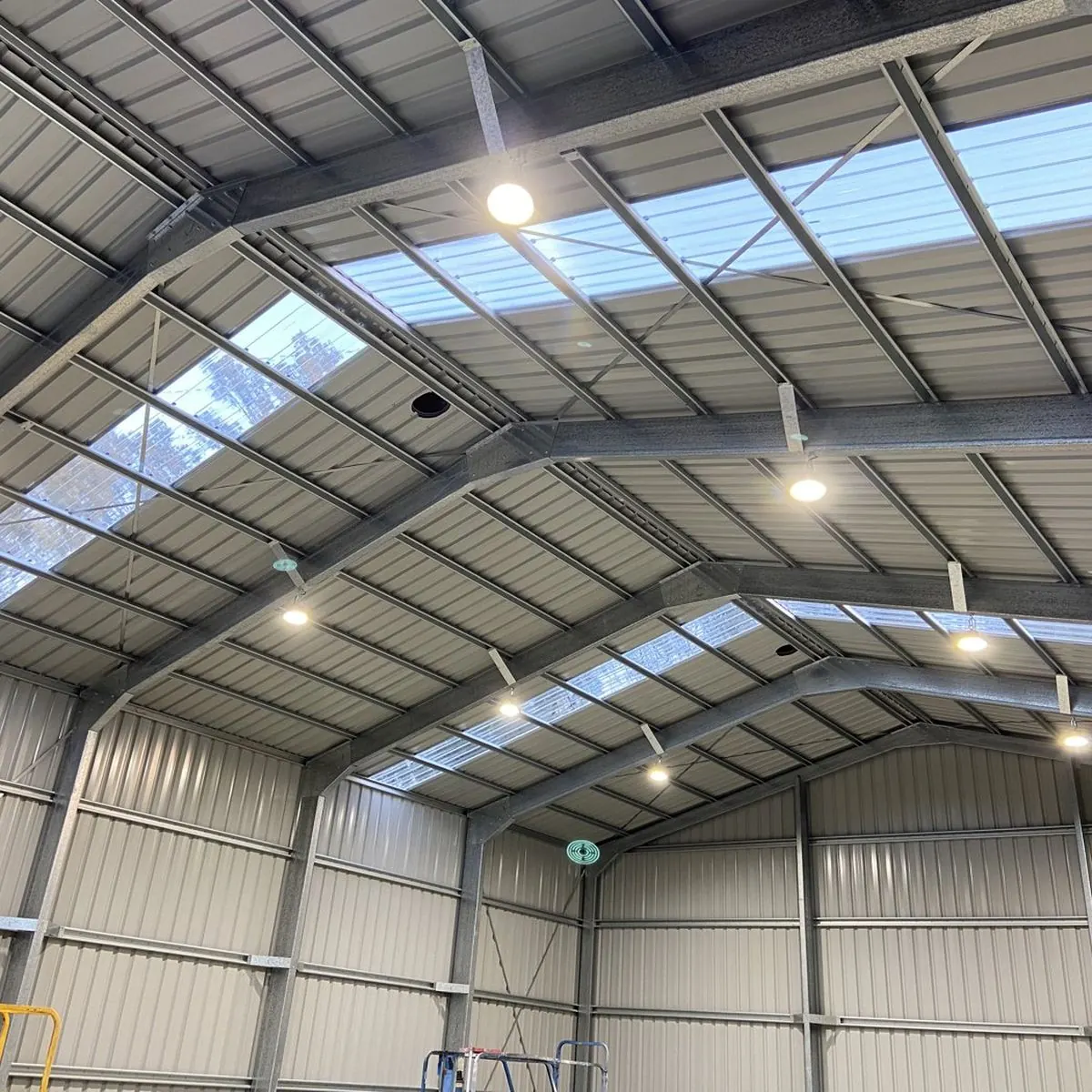 Rows of ceiling lights installed along the roof of a large steel shed