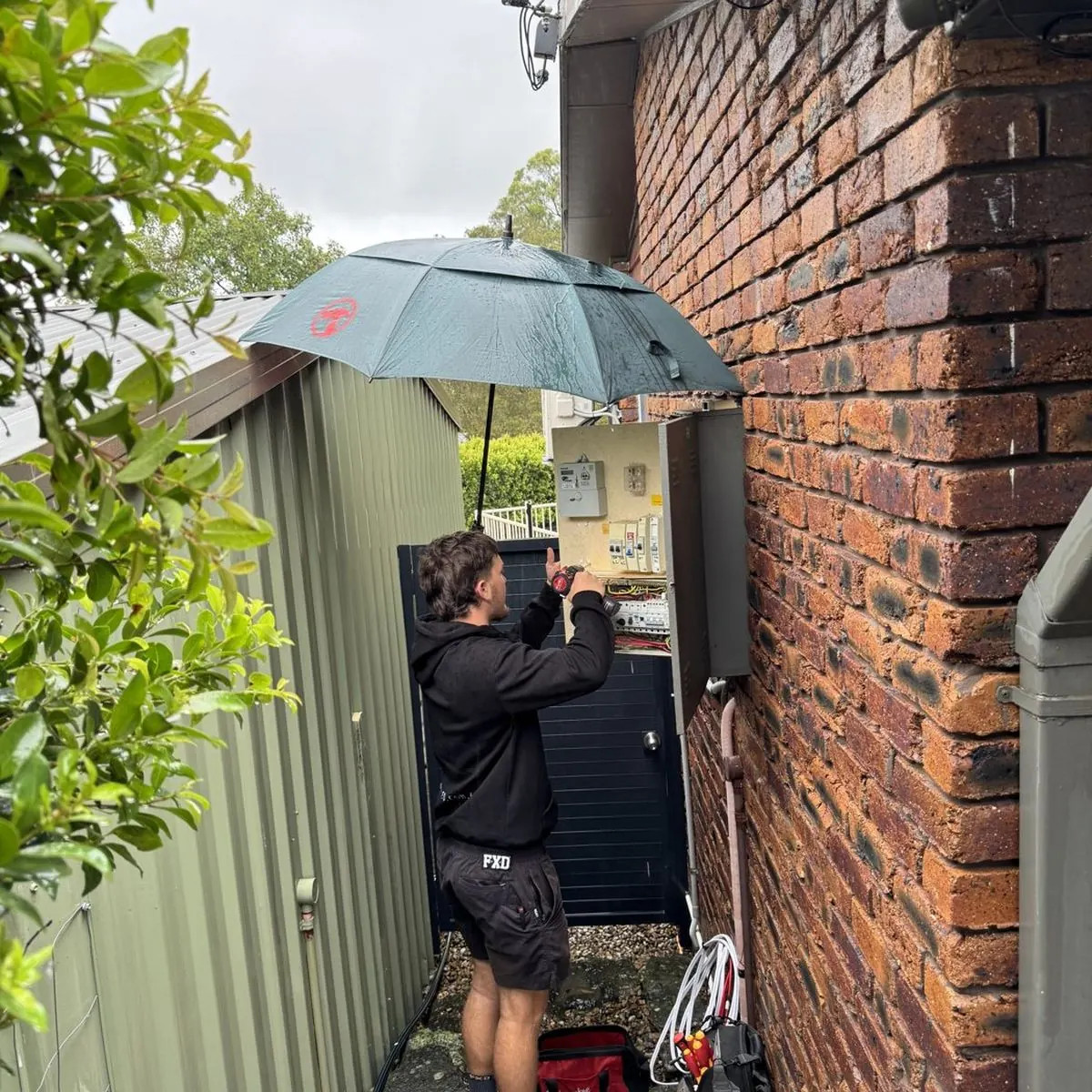 An electrician working on an open outdoor switchboard with an umbrella rigged over it